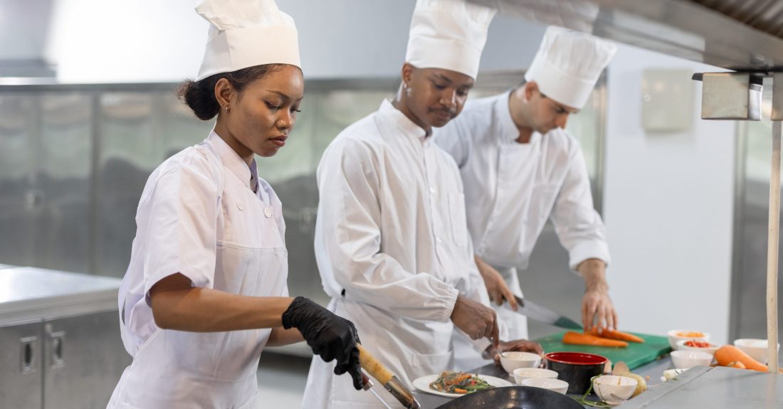 Group of chefs smiling and working together in professional kitchen, preparing, plating dishes with joy. Great for concepts like culinary teamwork, chef training, kitchen lifestyle restaurant culture.